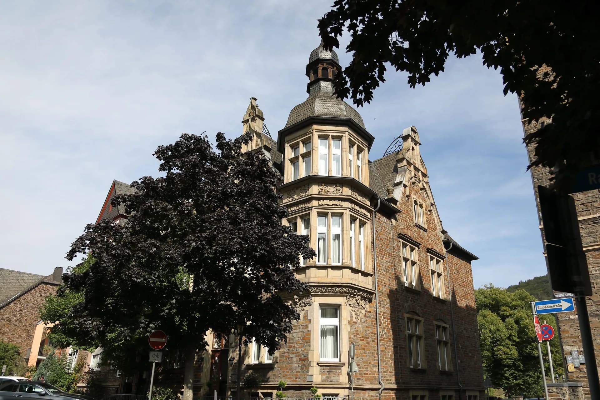 Turm und Giebel der Moselvilla zwischen Bäumen an der Straße