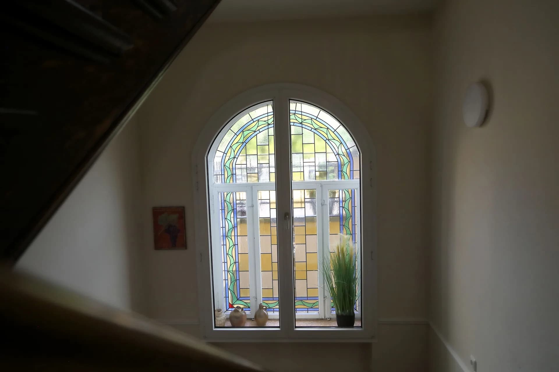 Buntglasfenster im Treppenhaus mit dekorativen Tonkrügen auf der Fensterbank