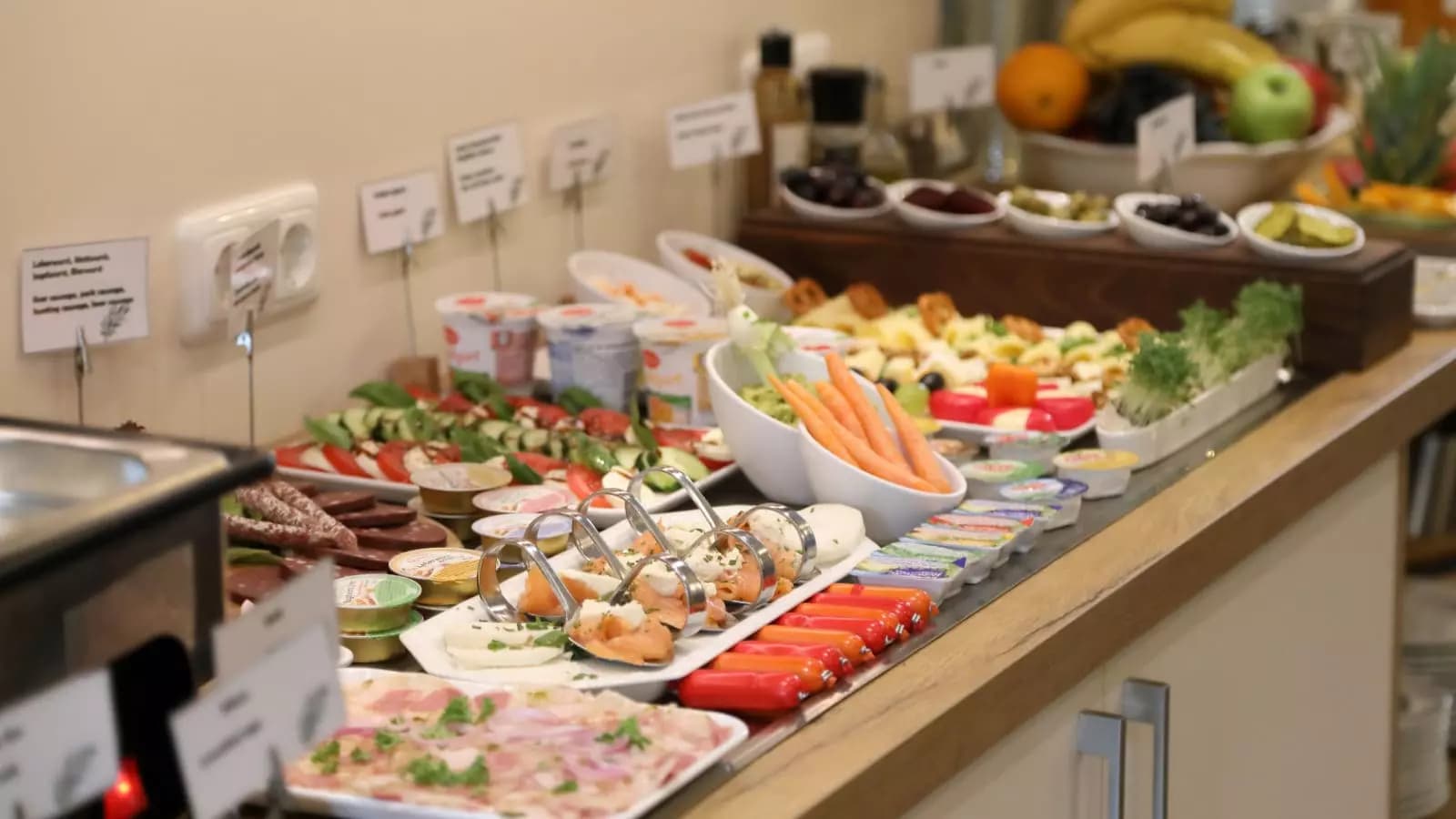Reichhaltiges Frühstücksbuffet mit Käse, Aufschnitt, frischem Gemüse und Joghurt