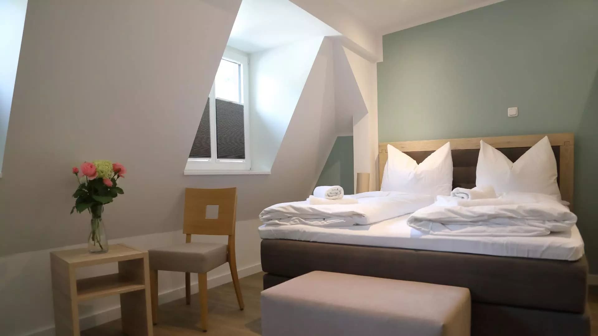 Zimmer unter dem Dach mit Dachschrägen, Boxspringbett und frischem Blumenstrauß