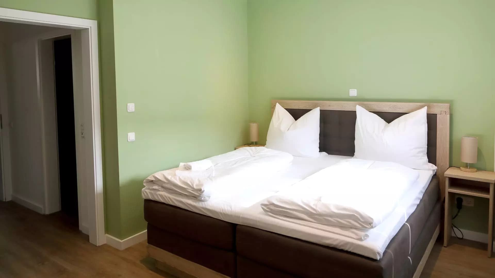 Doppelzimmer mit grüner Wandfarbe, Boxspringbett und weißer Bettwäsche