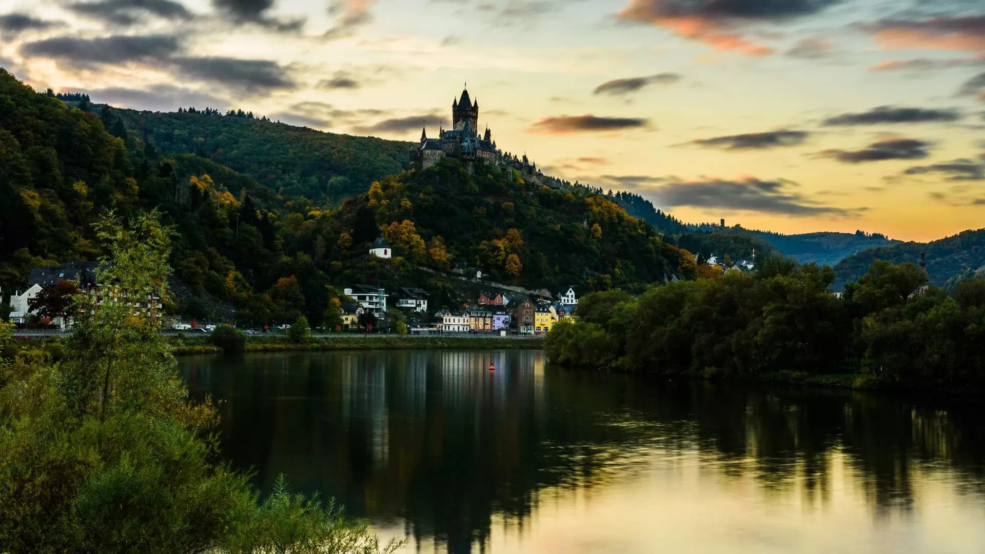 Reichsburg Cochem hoch über der Mosel im Abendlicht mit bunten Häusern am Ufer