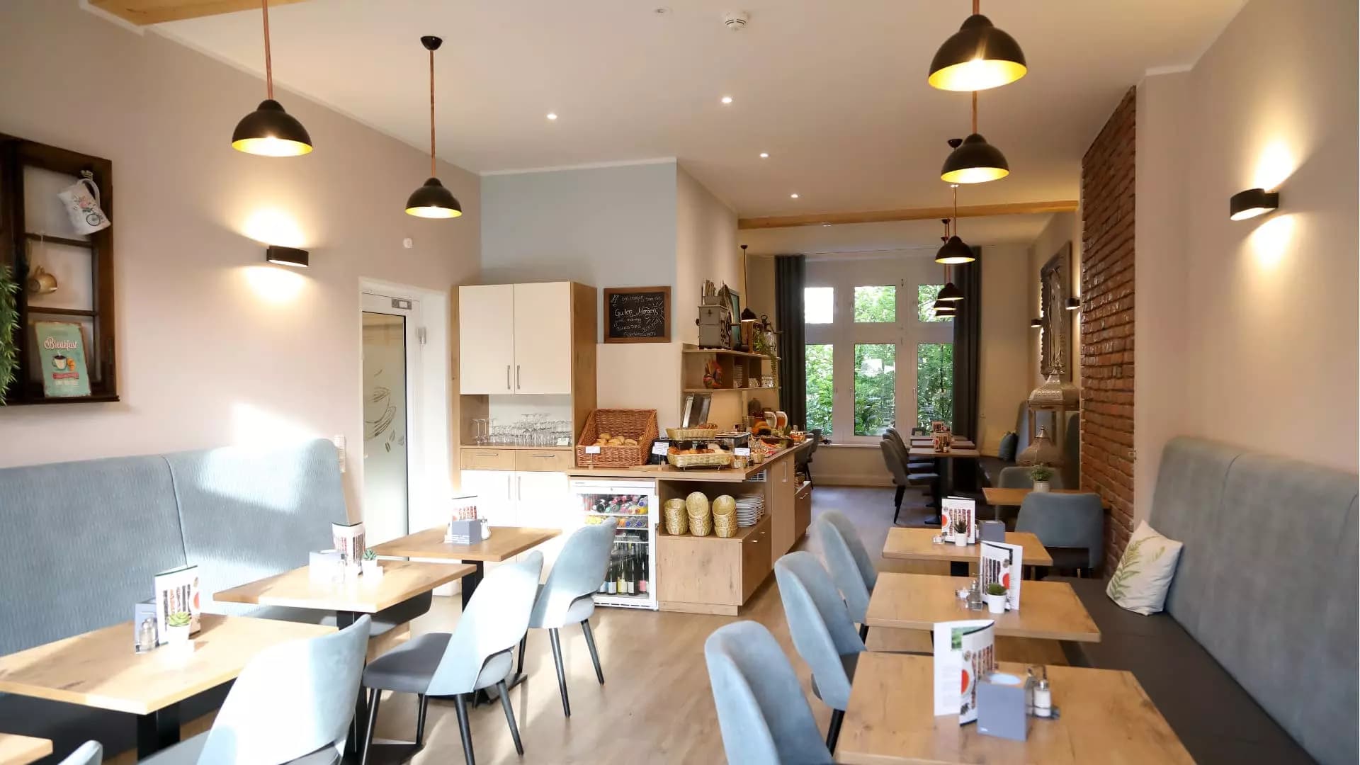 Frühstücksraum mit Pendelleuchten, gepolsterten Sitzbänken und Blick zur Buffettheke
