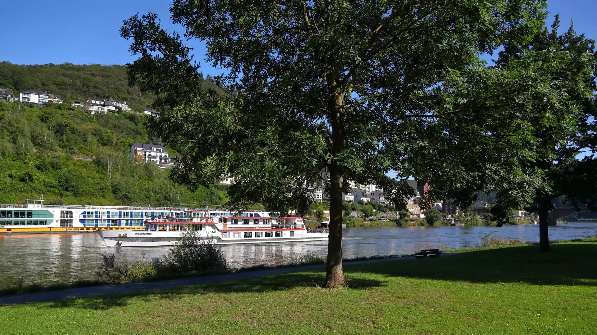 Moselpromenade mit vorbeifahrendem Ausflugsschiff und Blick auf die Hügel bei Cochem