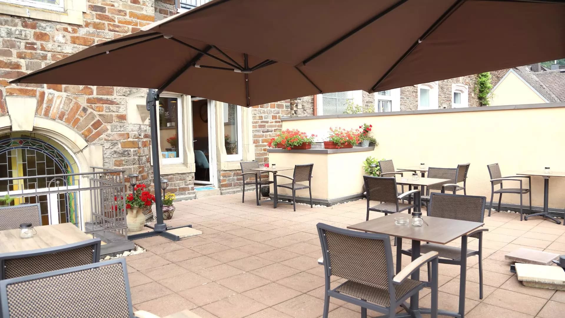 Terrasse mit Sonnenschirm, roten Geranien und gemütlichen Sitzgruppen im Innenhof